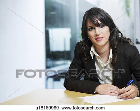 Stock Photo - Young businesswoman sitting in office, smiling, portrait. Fotosearch