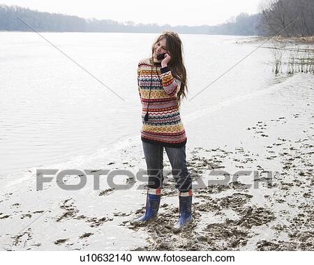 Young woman standing by river, using mobile phone, smiling View Large Photo Image Stock Image - Young woman standing by river, using mobile phone, smiling. Fotosearch