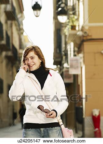 Stock Photo - Young woman using mobile phone in street, smiling. Fotosearch