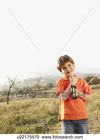 Stock Image - Boy (4-6) holding kite in field, smiling, portrait. Fotosearch