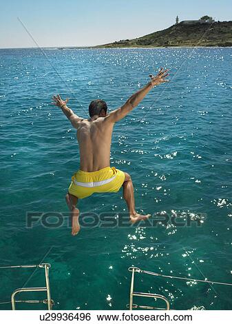Stock Photograph - Man jumping into sea from boat, rear view. Fotosearch