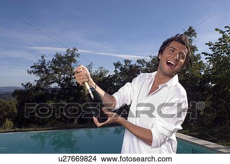 Man opening a bottle of champagne by a pool View Large Photo Image Picture - Man opening a bottle of champagne by a pool. Fotosearch