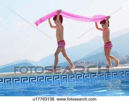 Stock Photo - Two brothers (5-7) carrying inflatable by outdoor swimming pool. Fotosearch