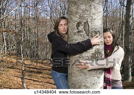 Two young women hugging a tree. View Large Photo Image Picture - Two young women hugging a tree.. Fotosearch