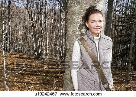 Stock Photo - Woman leaning against a tree smiling.. Fotosearch