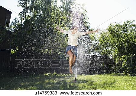 Stock Image - Women jumping over garden sprinkler.. Fotosearch
