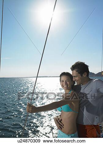 Stock Photo - Young couple standing on yacht at sea, smiling. Fotosearch