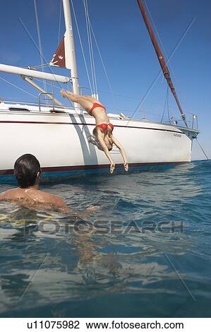 Stock Image - Young woman diving into sea from yacht, man in foreground. Fotosearch
