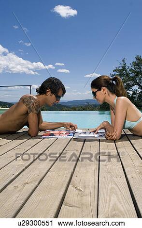 Couple sunbathing by a swimming pool with magazines View Large Photo Image Stock Image - Couple sunbathing by a swimming pool with magazines. Fotosearch