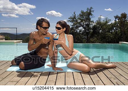 Stock Photography - Couple sunbathing by a swimming pool with drinks. Fotosearch