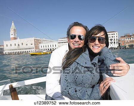 Stock Image - Italy, Venice, couple wearing sunglasses on boat, smiling. Fotosearch