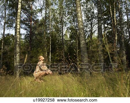 Stock Photo - Woman crouching on a large rock in forest smiling.. Fotosearch