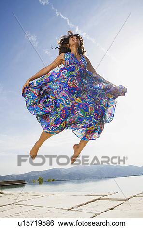 Woman jumping by an infinity pool in a colorful dress smiling. View Large Photo Image Stock Photograph - Woman jumping by an infinity pool in a colorful dress smiling.. Fotosearch