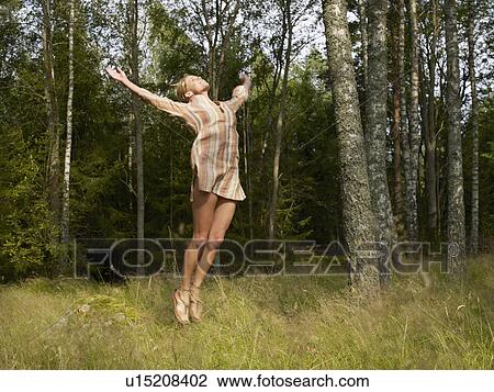 Stock Image - Woman jumping in a forest smiling.. Fotosearch