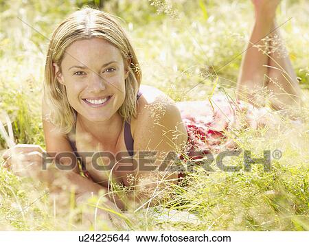 Picture - Woman lying in grass smiling.. Fotosearch