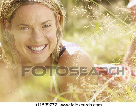 Stock Image - Woman lying in grass smiling.. Fotosearch