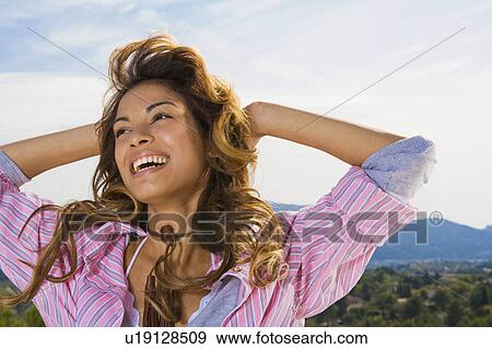 Stock Photo - Woman smiling with hands behind head outdoors.. Fotosearch