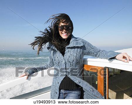 Stock Image - Woman wearing sunglasses on boat, smiling. Fotosearch
