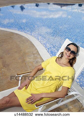 Woman wearing sunglasses relaxing on sun lounger, smiling View Large Photo Image Stock Image - Woman wearing sunglasses relaxing on sun lounger, smiling. Fotosearch