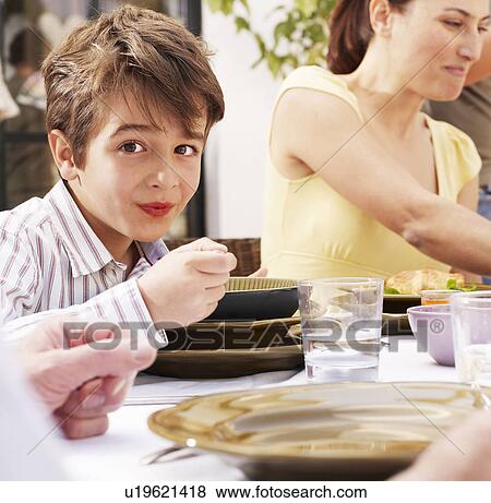 Stock Photo - Boy (4-6) having meal with family, smiling, portrait. Fotosearch