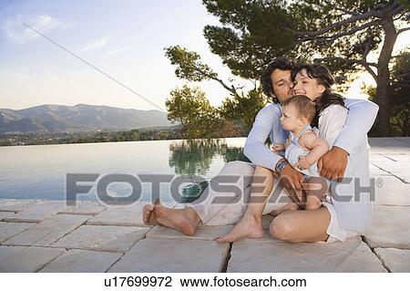 Stock Image - Family by a pool embracing and smiling.. Fotosearch