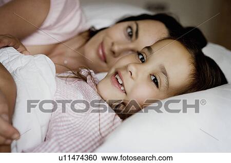 Stock Image - Mother and daughter sitting on a bed.. Fotosearch