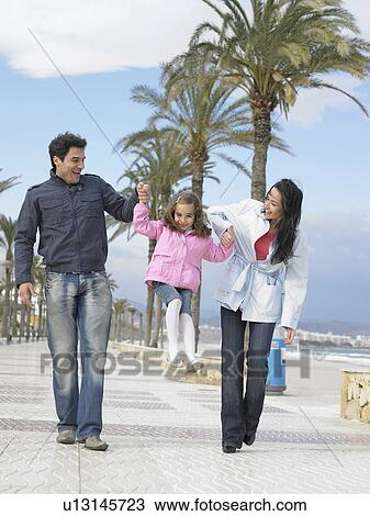 Mother and father walking along palm lined pavement by the sea swinging young daughter (6-8). Alicante, Spain. View Large Photo Image Stock Image - Mother and father walking along palm lined pavement by the sea swinging young daughter (6-8). Alicante, Spain.. Fotosearch