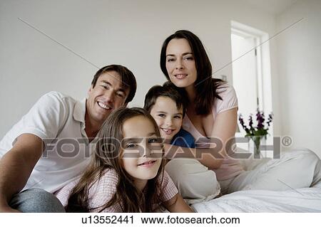 Portrait of a family sitting on a bed. View Large Photo Image Stock Image - Portrait of a family sitting on a bed.. Fotosearch