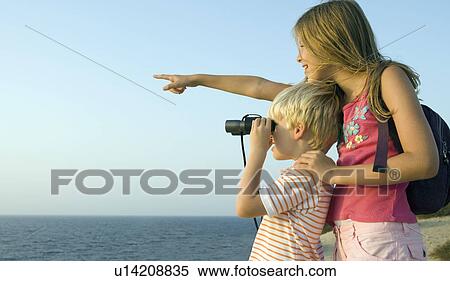 Young girl pointing out over the sea smiling with young boy using binoculars. View Large Photo Image Stock Photography - Young girl pointing out over the sea smiling with young boy using binoculars.. Fotosearch
