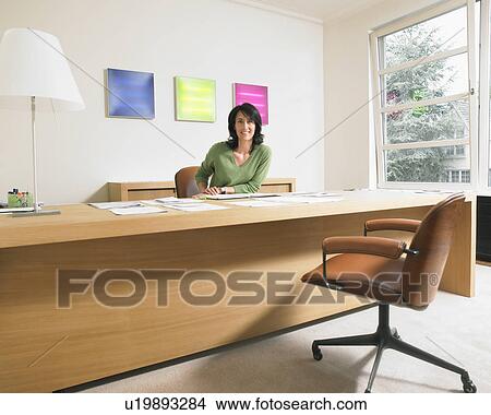 Smiling businesswoman looking at camera at her desk. View Large Photo Image Picture - Smiling businesswoman looking at camera at her desk.. Fotosearch