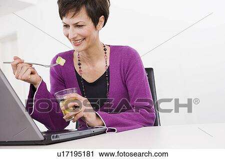 Stock Image - Woman eating in front of her pc. Fotosearch