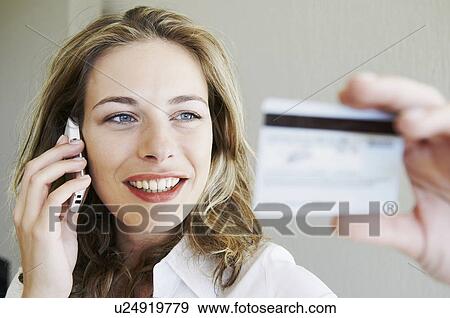 Stock Photo - Woman on phone, looking at credit card. Fotosearch