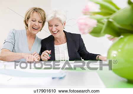Stock Image - Women laughing, looking at papers. Fotosearch