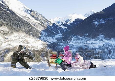 Stock Image - Children playing in snow with presents. Fotosearch