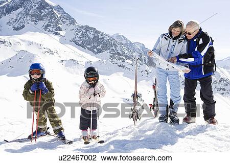 Stock Image - Grandparents reading piste map with kids. Fotosearch