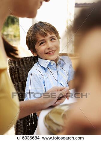 Picture - Boy (4-6) sitting at table with family in garden, smiling. Fotosearch