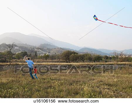 Stock Photograph - Father and son (4-6) running in a field with kite. Fotosearch