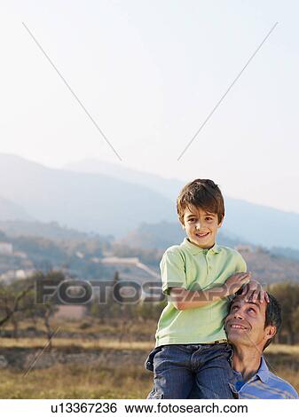 Stock Photograph - Father carrying son (4-6) on shoulder, smiling. Fotosearch