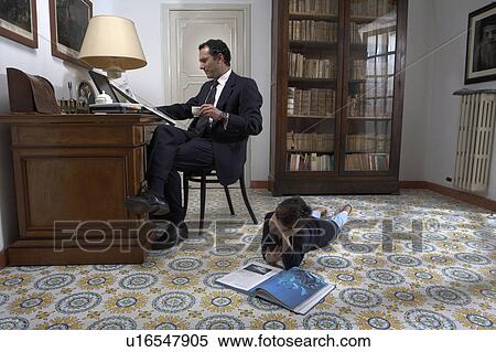Stock Photography - Father sitting looking at laptop and son (4-6) reading book. Fotosearch