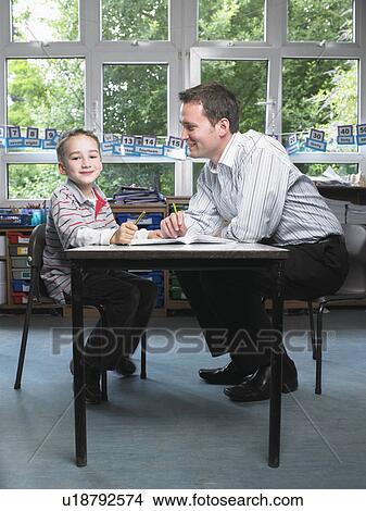 Male teacher helping young boy with work in classroom View Large Photo Image Picture - Male teacher helping young boy with work in classroom. Fotosearch