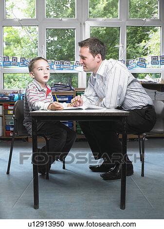Stock Image - Male teacher helping young boy with work in classroom. Fotosearch