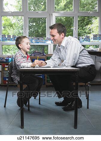 Male teacher helping young boy with work in classroom View Large Photo Image Stock Photography - Male teacher helping young boy with work in classroom. Fotosearch