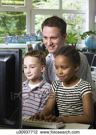 Stock Image - Male teacher looking at computer monitor with boy and girl. Fotosearch