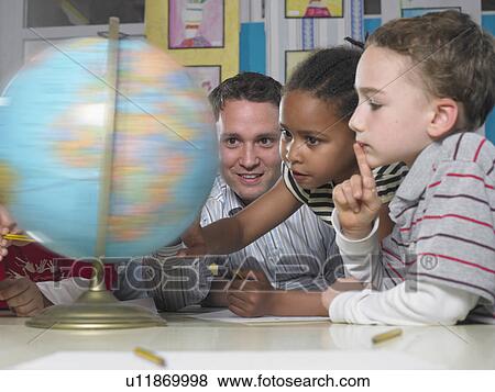 Stock Photo - Male teacher looking at spinning globe with boy and girl. Fotosearch