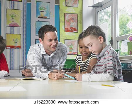 Male teacher sitting at work table with girl and boy View Large Photo Image Stock Image - Male teacher sitting at work table with girl and boy. Fotosearch
