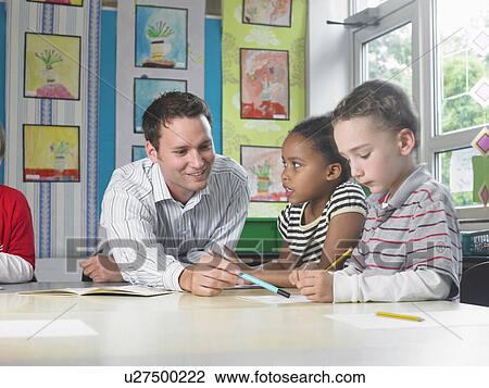 Male teacher sitting at work table with girl and boy View Large Photo Image Stock Image - Male teacher sitting at work table with girl and boy. Fotosearch