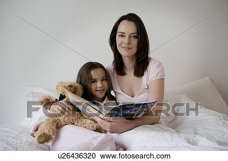 Stock Image - Mother and daughter sitting on a bed.. Fotosearch