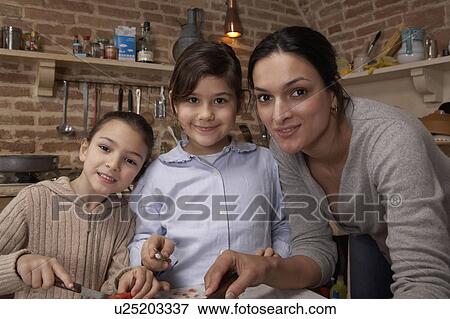 Stock Photo - Mother and two daughters (5-8) in kitchen, portrait. Fotosearch