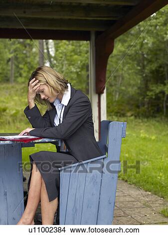 Picture - Businesswoman sitting on bench by house. Fotosearch