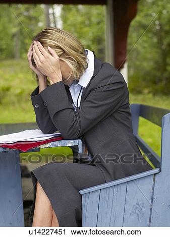 Stock Image - Businesswoman sitting on bench by house. Fotosearch